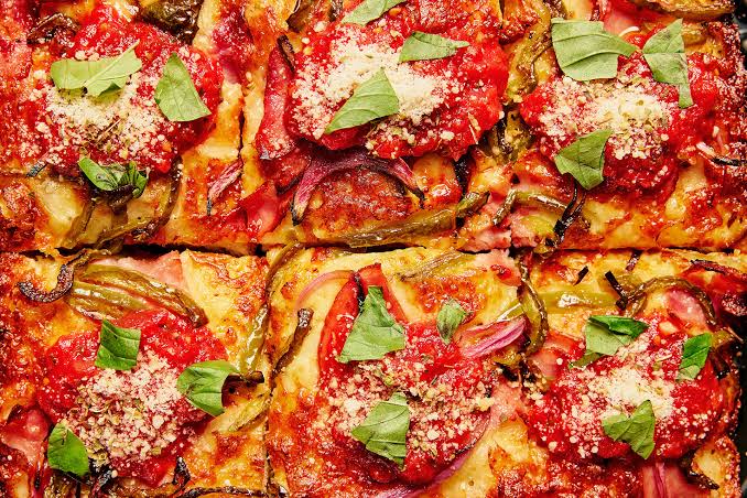 Close view of square Detroit-style pizzas topped with red sauce and basil